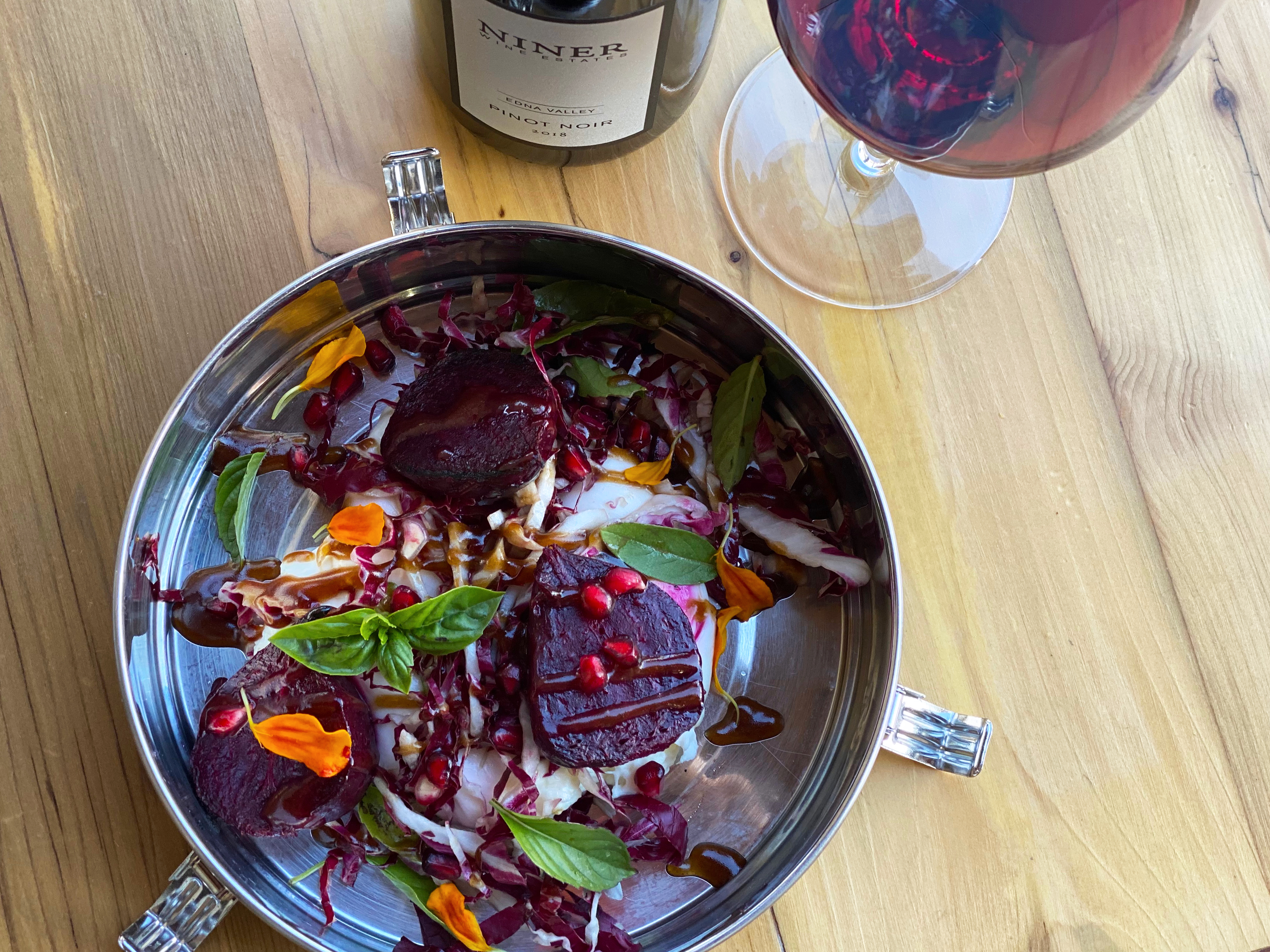 Seasonal burrata dish with beets, pomegranate seeds, basil, radicchio and edible flowers in a metal tiffin.