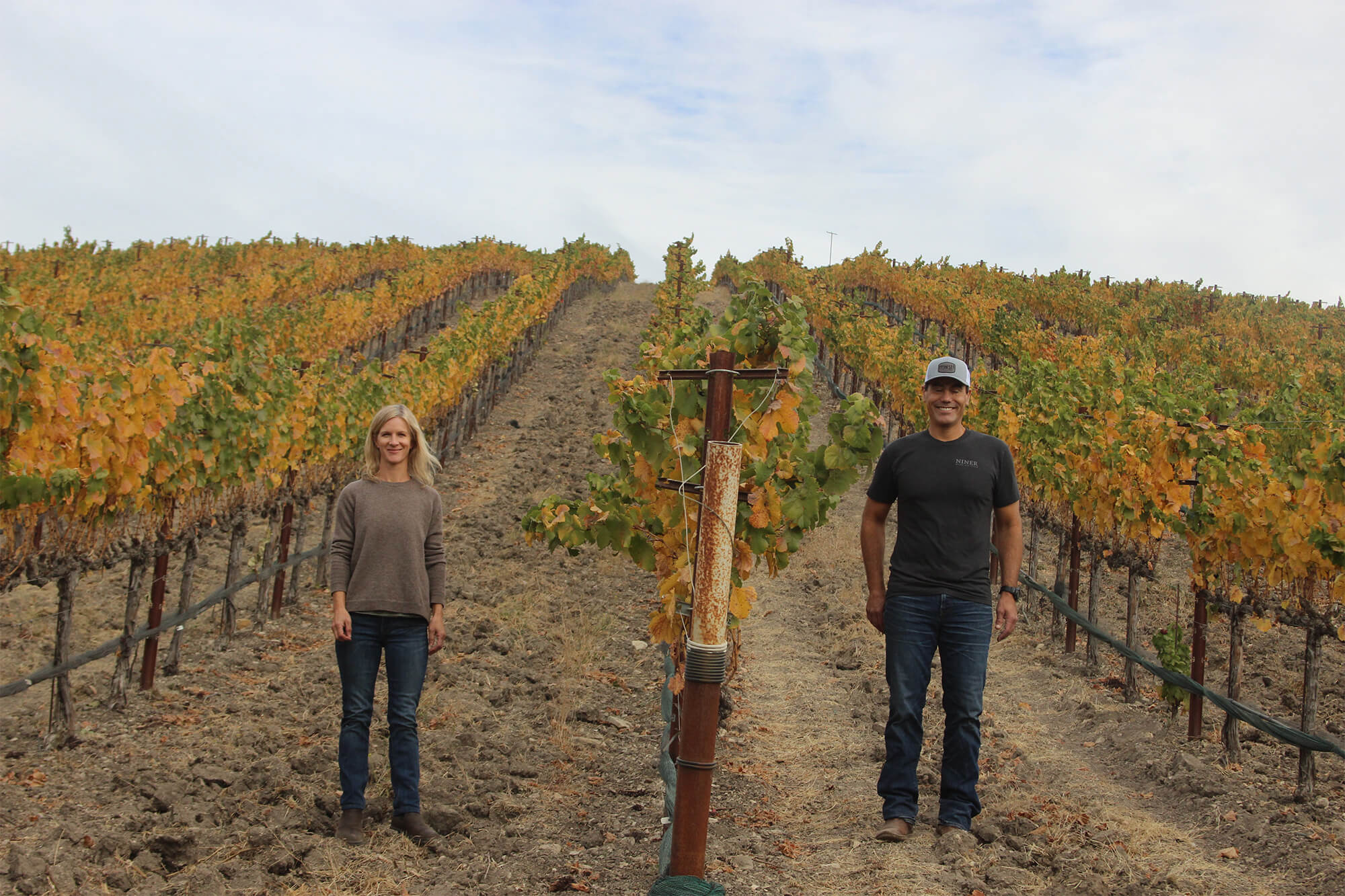 Winemakers Molly Bohlman & Patrick Muran standing between colorful fall vineyard rows at Heart Hill Vineyard.