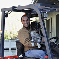 Winemaker Patrick Muran sitting on a fork lift holding his dog 