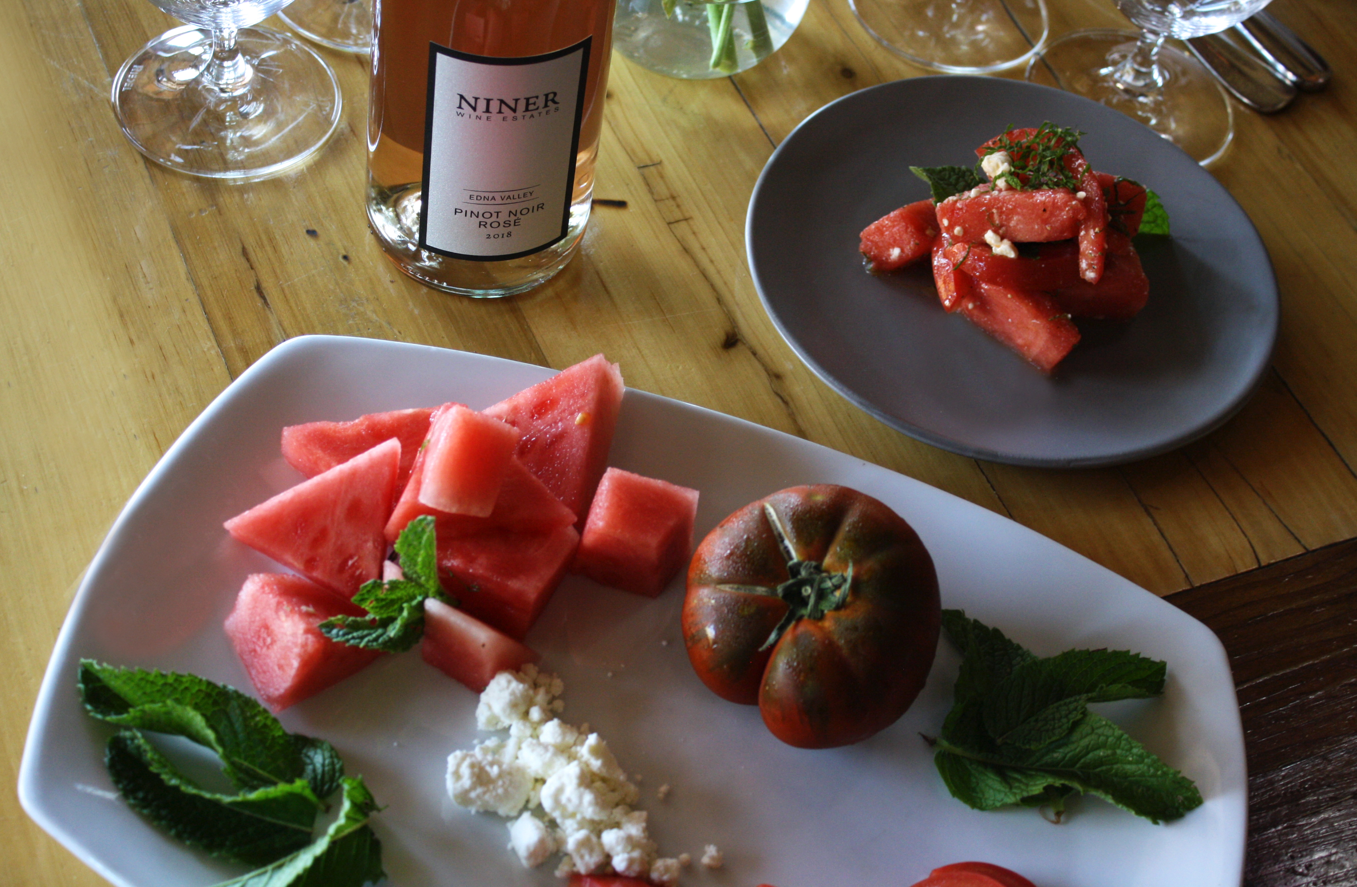 Ingredients for watermelon salad on a white plate with a glass and bottle of Rose